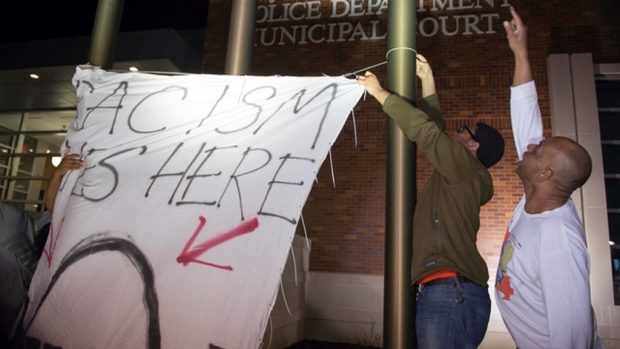 Demonstranti před policejní stanicí ve Fergusonu pověsili nápis: &quot;Zde žije rasismus&quot;