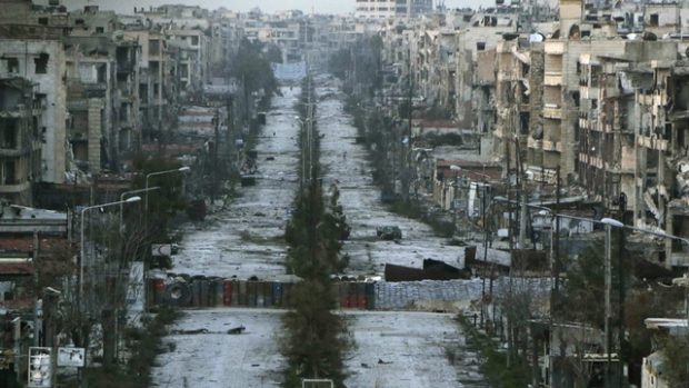 Pohled ukazuje zničenou ulici ve městě Aleppo, na které jsou jako bariéry vyskládané pytle s pískem
