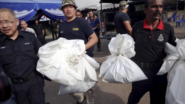 Malajsijští policisté s pravděpodobně lidskými ostatky, které se našly v hrobech poblíž hranice s Thajskem
