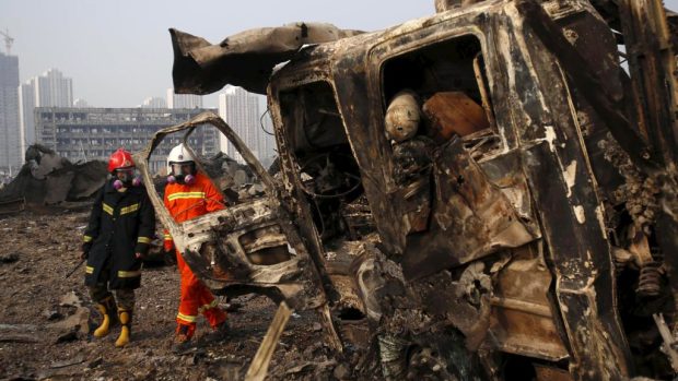 Hasiči procházejí kolem nákladního auta zničeného mohutným výbuchem v Tchien-ťinu