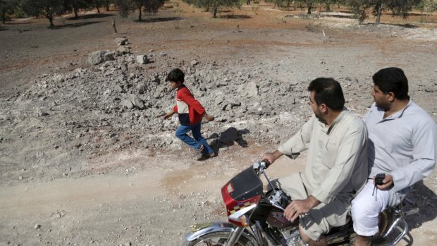 Civilisté poblíž města Al-Ghadfa jedou kolem kráteru, na svědomí ho údajně má nálet ruských letounů