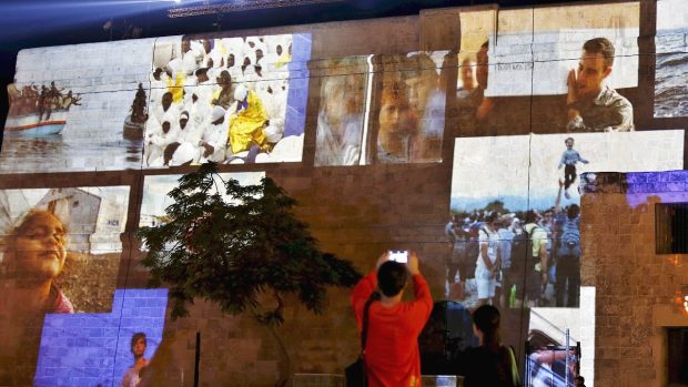 Obyvatelé Valetty si fotí projekci zobrazující uprchlíky během zkoušky slavnostního zahájení summitu