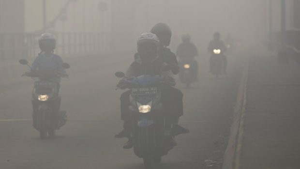 Lidé na motorkách na jihu Bornea se prodírají dýmem z hořících deštných lesů