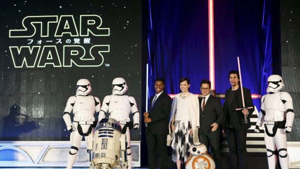 Star Wars. Zleva bílí vojáci Impéria, takzvaní stormtroopeři, herci  John Boyega a Daisy Ridleyová, režisér J. J. Abrams a herec Adam Driver. V popředí vlevo robot R2-D2 a vpravo nový BB-8