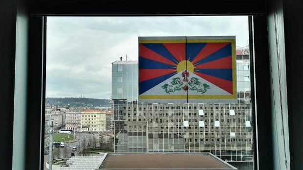 Za tibetskou vlajkou je na střeše hotelu vidět policista se zbraní