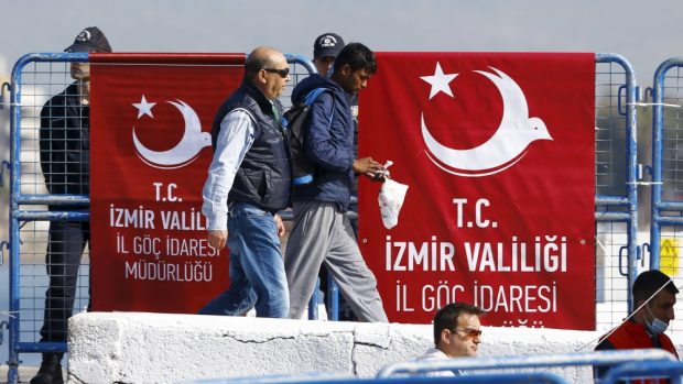 Turecký policista doprovází běžence po připlutí z Lesbu do přístavu v Dikili