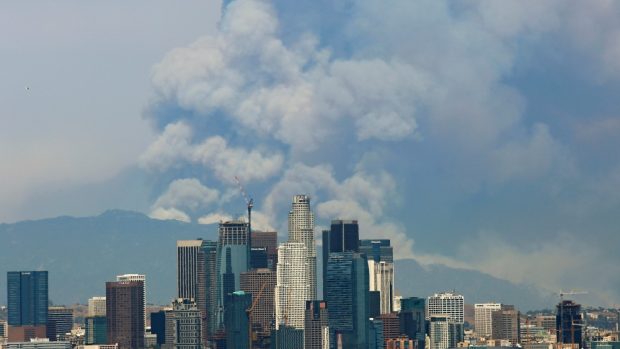 Nad siluetou Los Angeles vystupuje dým z lesního požáru na pokraji metropole
