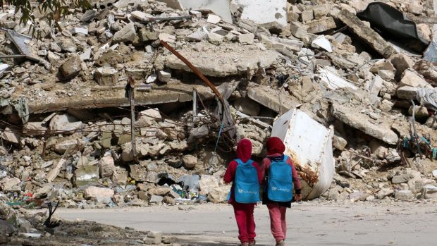 Děti procházejí zničenou čtvrtí syrského Aleppa