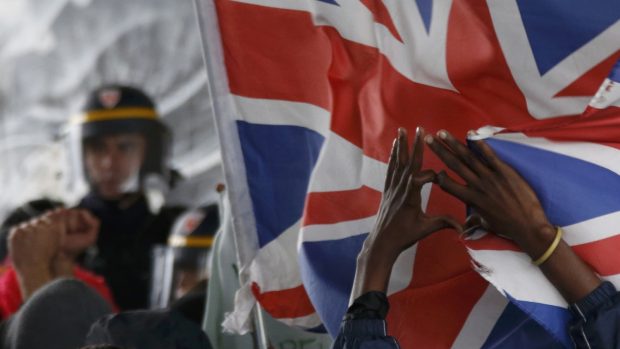 Protestující nedaleko uprchlického tábora v Calais drží britskou vlajku