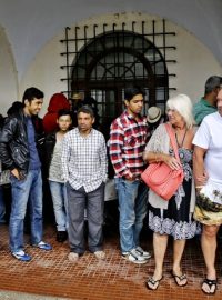 Uprchlíci a turisté se schvávají před deštěm u policejní stanice na ostrově Kos