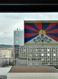 Za tibetskou vlajkou je na střeše hotelu vidět policista se zbraní