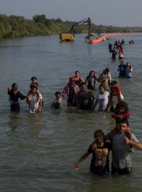 Běženci v řece Rio Grande se brodí kolem bójí, které je mají odradit od překročení hranice mezi USA a Mexikem