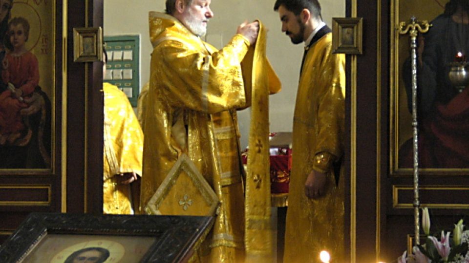 Skrze svaté dveře ikonostasu vidět biskup v plných liturgických rouchách barvy zlaté. V ruce drží epitrachil, který se chystá vložit na novosvěceného kněze. Ten má na sobě diákonský stichar a pod rukávy vidíme nárukávníky.